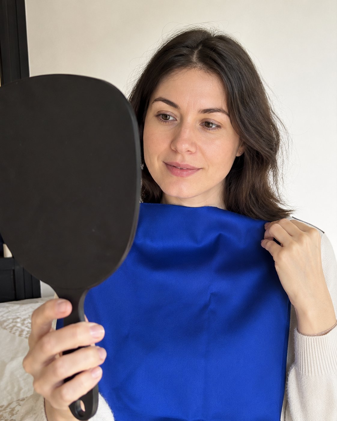 Donna con un drappo blu reale avvicinato al viso che si guarda in uno specchio a mano — test di draping armocromatico