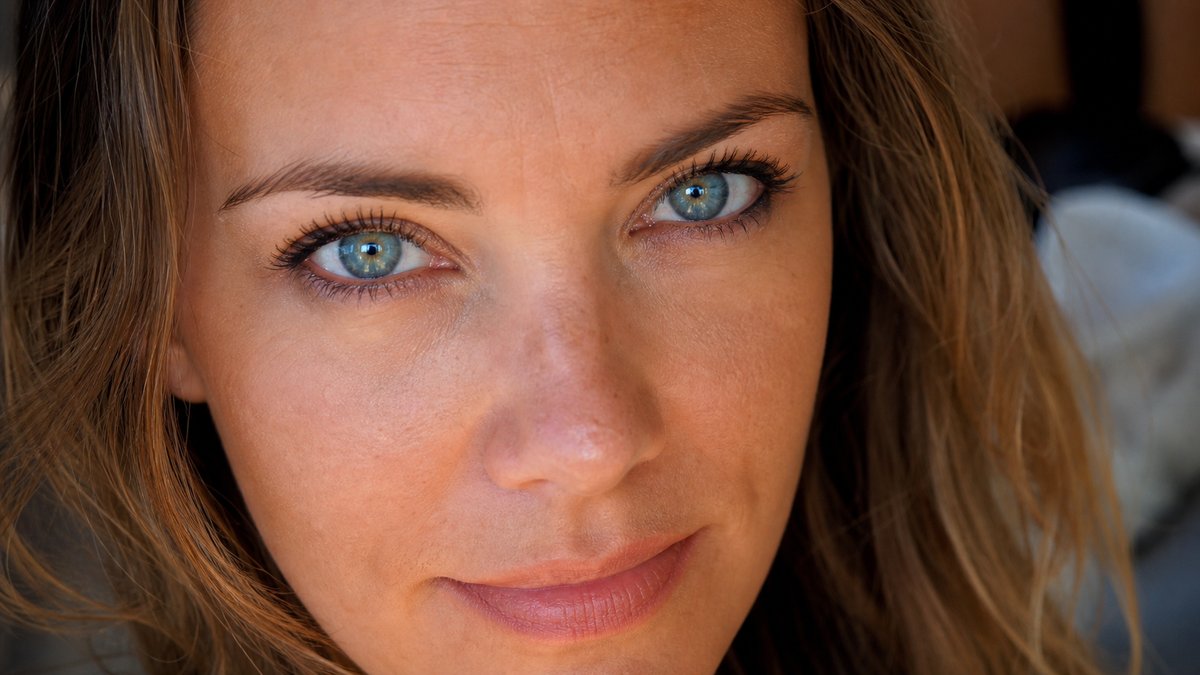 Primo piano di una donna con occhi azzurro-verde intensi e capelli castano dorato caldo, carnagione luminosa